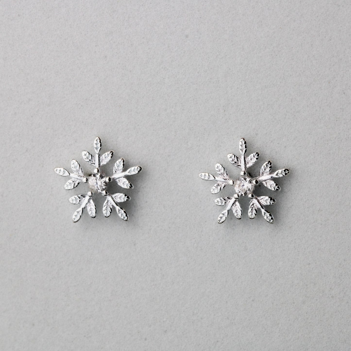 Silver snowflake shape stud earrings with a white crystal detail in the centre.