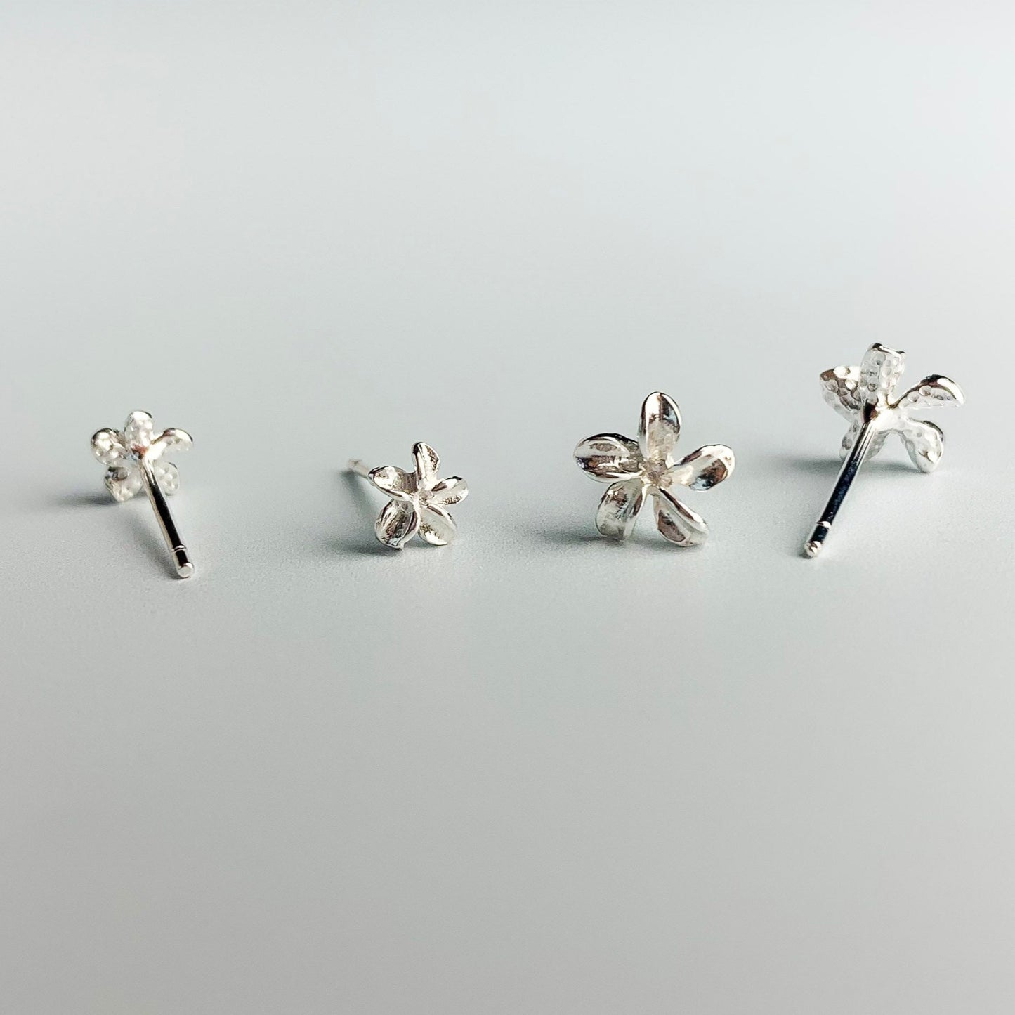 Two pairs of sterling silver flower stud earrings, in two different size options. They have a 3D moulded flower shape.