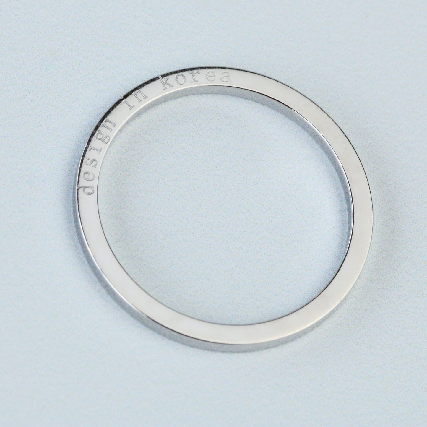 Silver ring with 'Dedicated to Korea' engraving on a light blue background