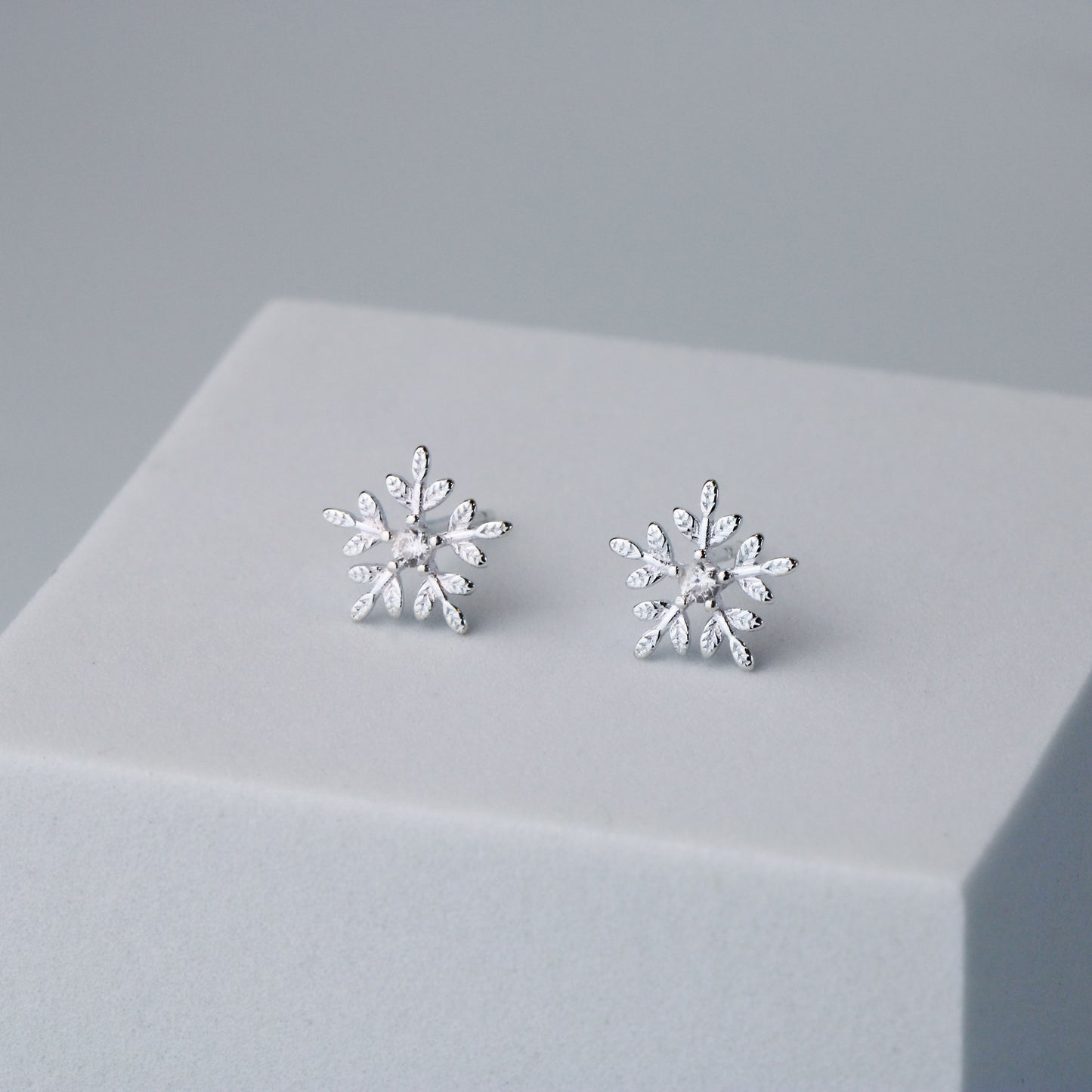 Silver snowflake shape stud earrings with a white crystal detail in the centre.