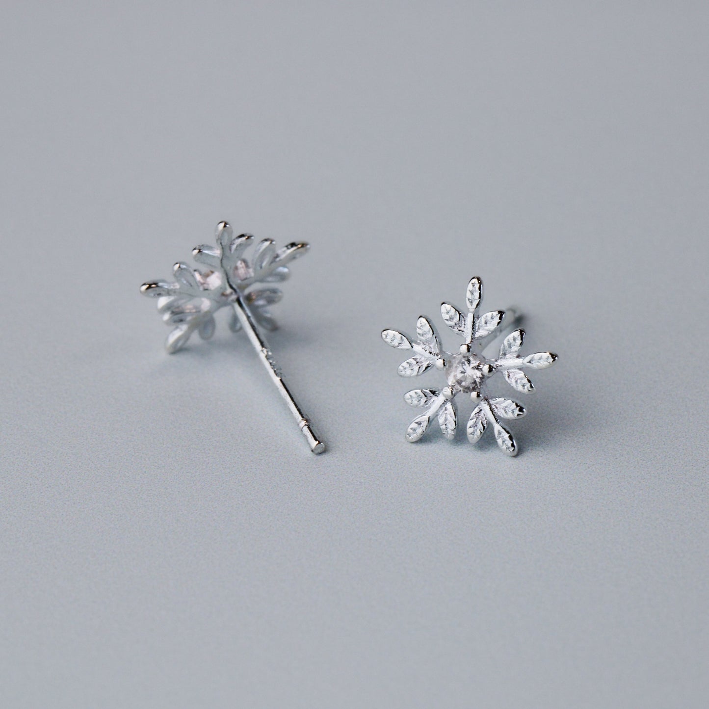 Silver snowflake shape stud earrings with a white crystal detail in the centre.