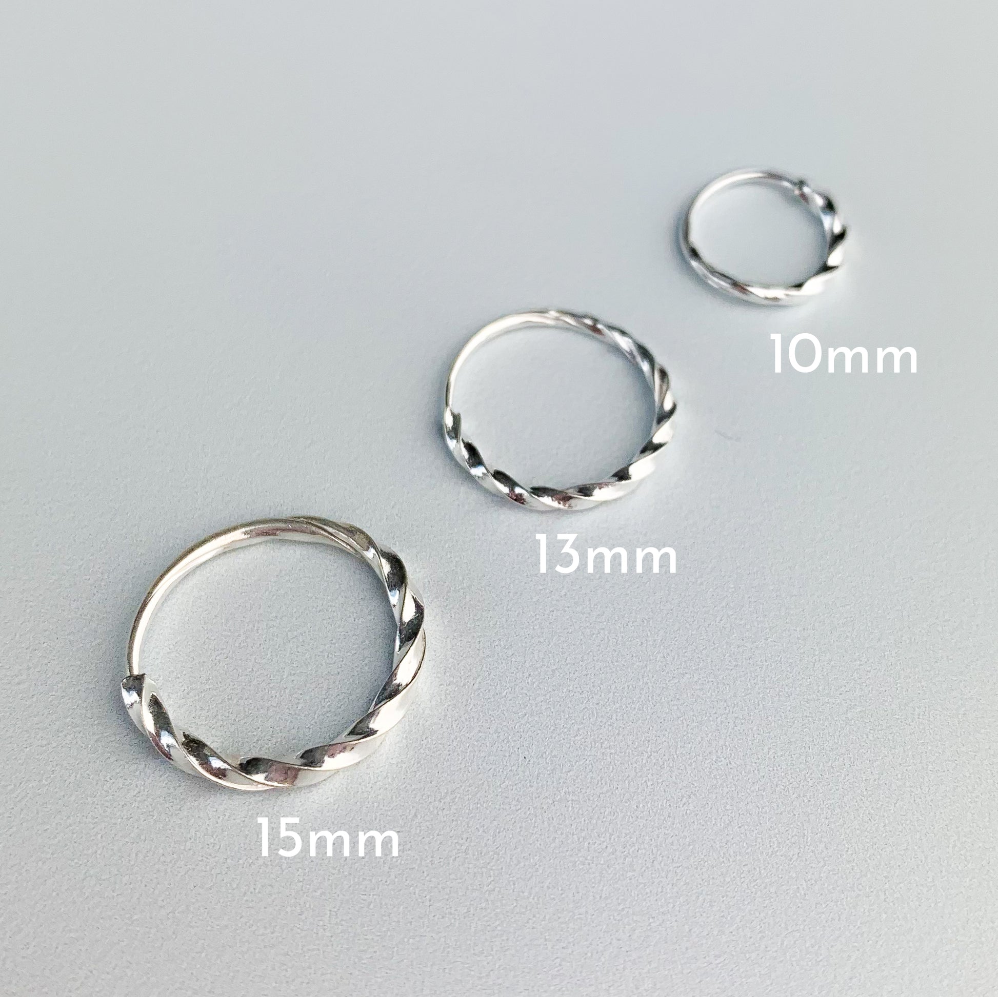Twisted silver hoop earrings with a sleeper fastening, in three sizes. The diameters are 15mm, 13mm, and 10mm