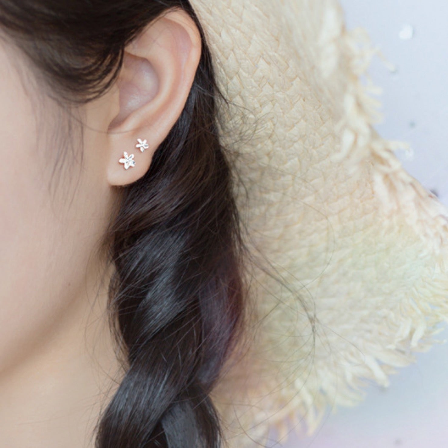 Model wearing two silver flower stud earrings in one ear, they are in two size options.